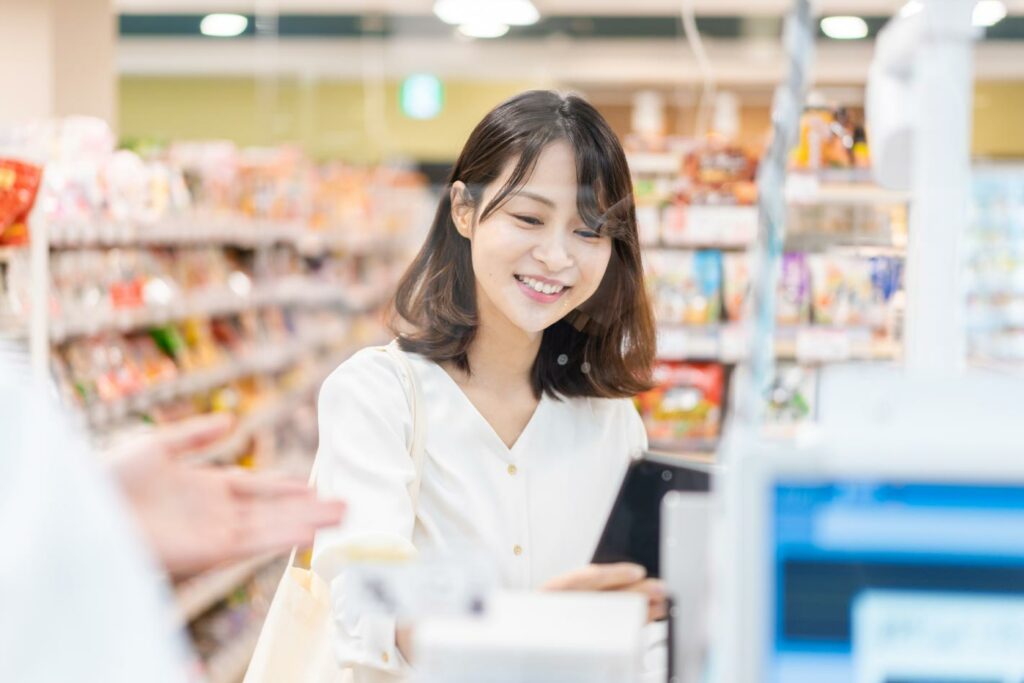 一位微笑的女性在日本超商結帳，正從自動收銀機取走收據。