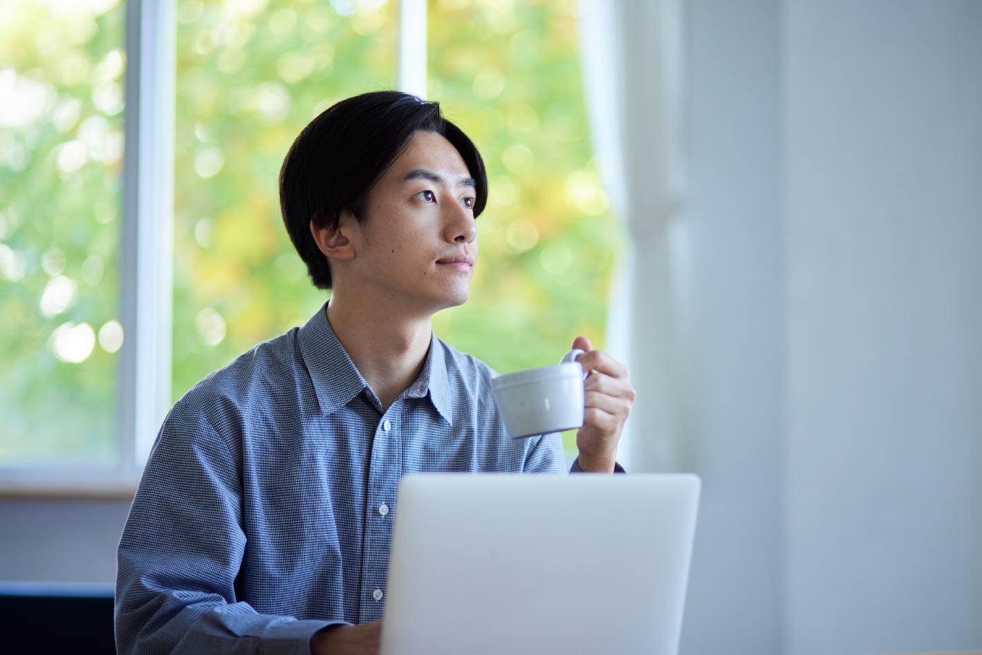 一名台灣男性上班族坐在辦公室內，手持一杯咖啡，目光遠望，似乎在沉思，筆記型電腦前展現出他的工作儀式感，透露出工作壓力與工作快樂間的平衡。